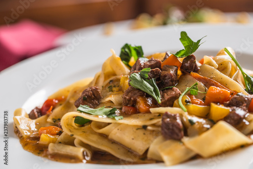 Idalian pasta pappardelle with beef ragu on white plate and red wine photo