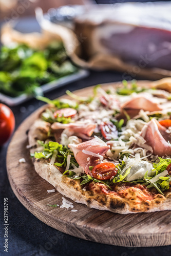 Italian pizza with prosciutto arugula tomatoes and parmesan on wooden round board