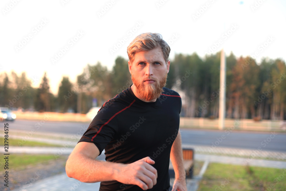 Fototapeta premium Fit athlete. Handsome adult man running outdoors to stay healthy, at sunset or sunrise. Runner.