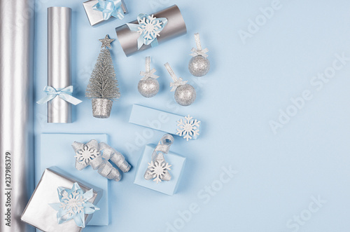 Modern soft minimalist christmas background with copy space - pastel blue and silver metallic gift boxes with shiny ribbons and bows on blue color backdrop, top view.