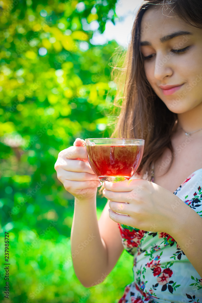 Young beautiful girl with long eye lashes with glass cup of black tea, happy teen girl smiling in floral summer dress drinking healthy herbal hot drink in garden, green nature, copy space Young beautiful girl with long eye lashes with glass cup of black tea, happy teen girl smiling in floral summer dress drinking healthy herbal hot drink in garden, green nature, copy space