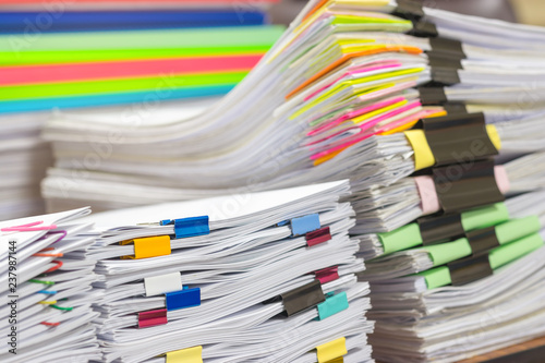 Pile of unfinished document on office desk. Stack of homework assignment archive with colorful paper and binder clip on teacher table waiting to be managed and checked. Education and business concept.