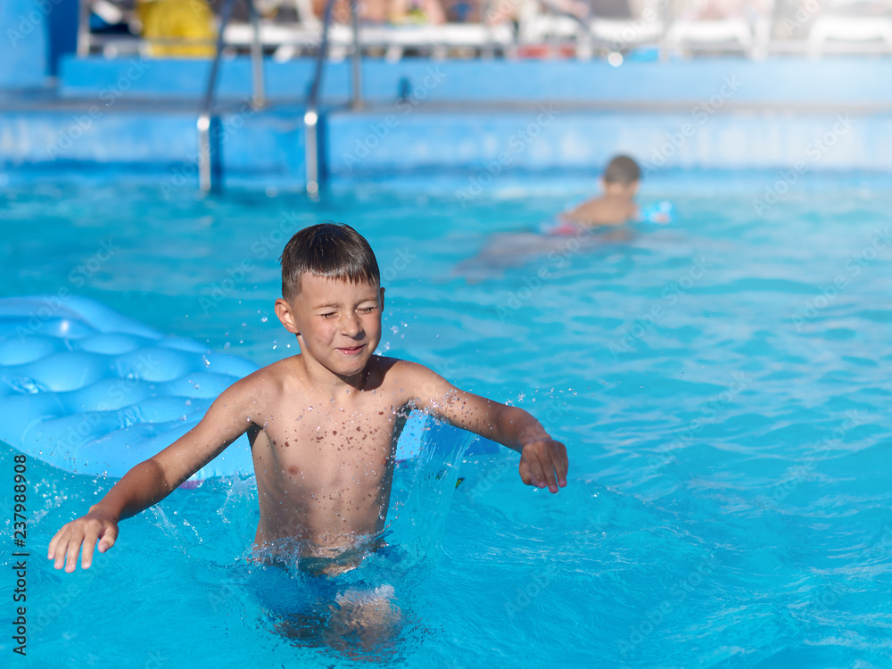 Smiling European boy is swimming on the inflatable blue floater in the hotel’s pool.