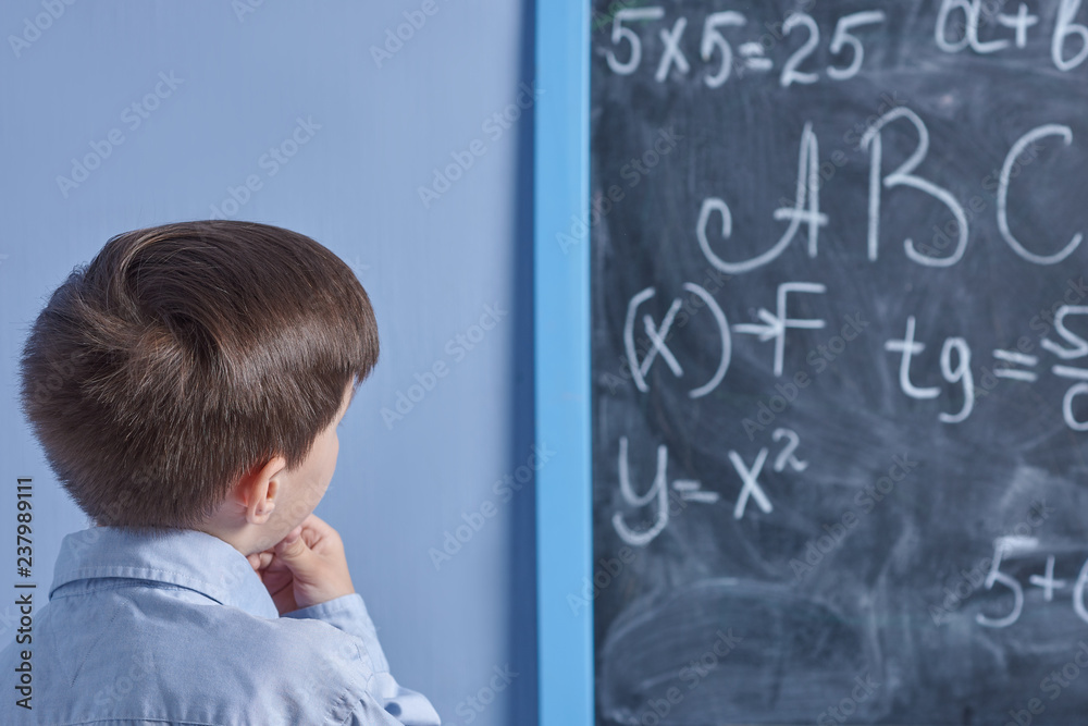 Smart European boy is standing at the blackboard and thinking over difficult mathematical problem, he is trying to solve it.