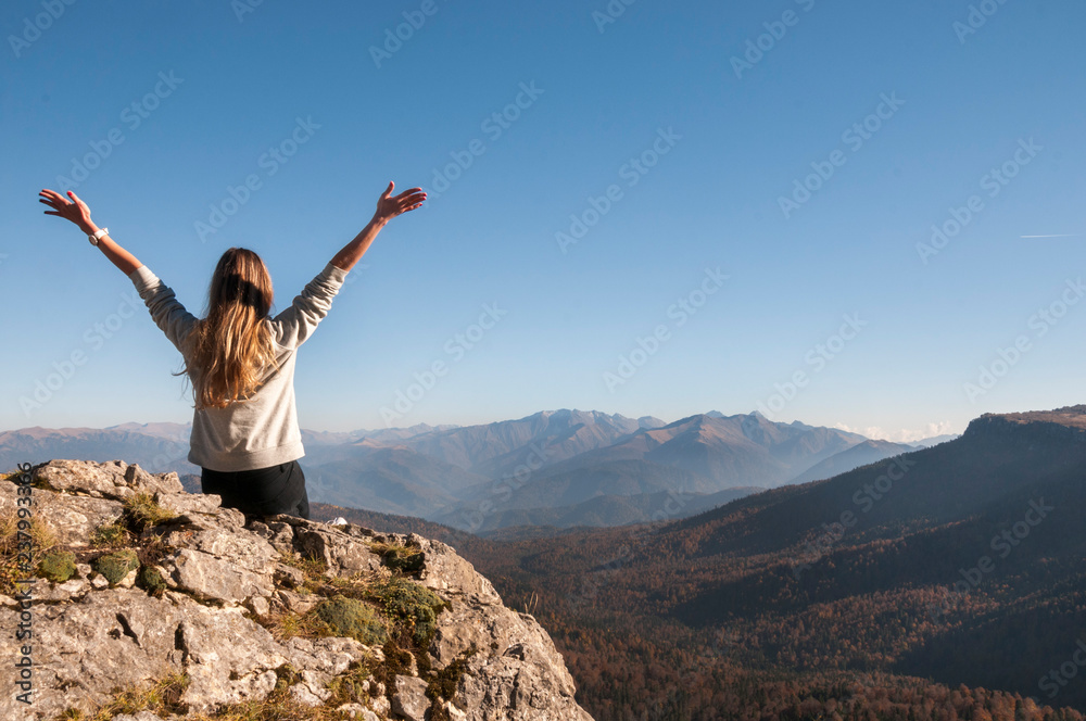 a young active girl sits on the edge of a rock, look at the Caucasus mountains. a young active girl sits on the edge of a rock, look at the Caucasus mountains.