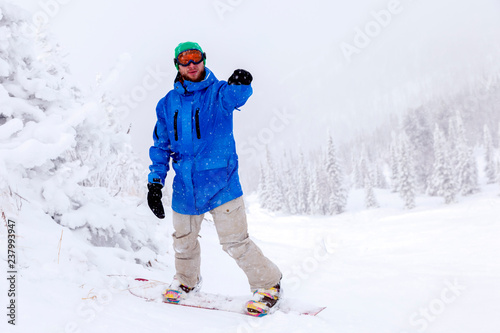 Professional man snowboarder in bright blue sportswear and outfit in snowy sunny high mountains. Concept of rest apres ski