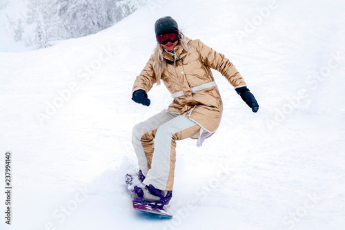 Professional woman snowboarder in golden sportswear riding on slope in snowy sunny high mountains. Blur, soft focus, object in motion. Concept of freeride
