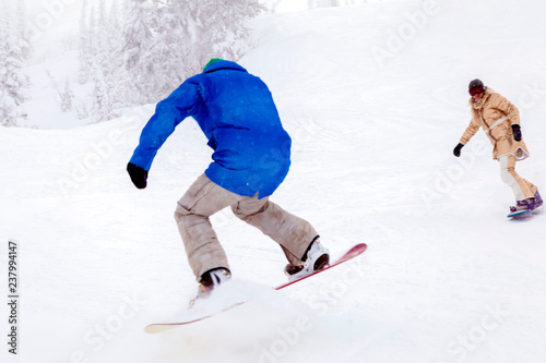 Couple of snowboarders in bright sportswear and outfit riding in snowy sunny high mountains. Blur, soft focus, object in motion. Concept honeymoon, outdoor rest