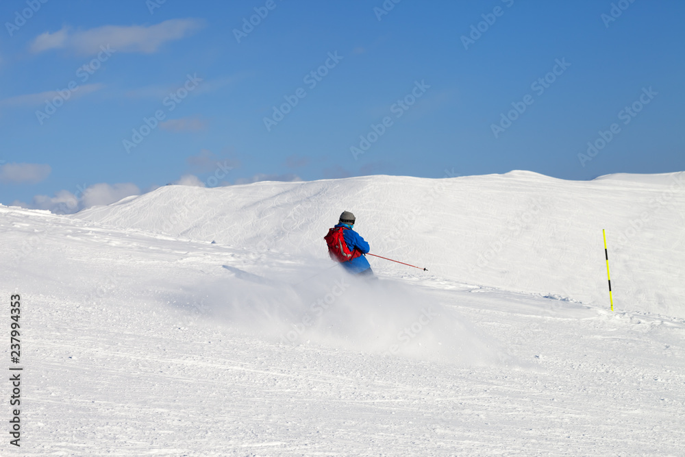 Skier downhill on snowy ski slope in sun winter day