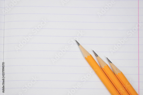 Notebook in the line. The notebook sheet occupies the entire space of the frame. On a notebook sheet three pencils. View from above. Close-up.