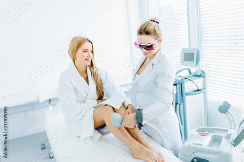 Young blonde female client chooses laser hair removal cosmetology procedure instead of waxing  talking with a therapist at cosmetic beauty spa clinic. Laser epilation and cosmetology.