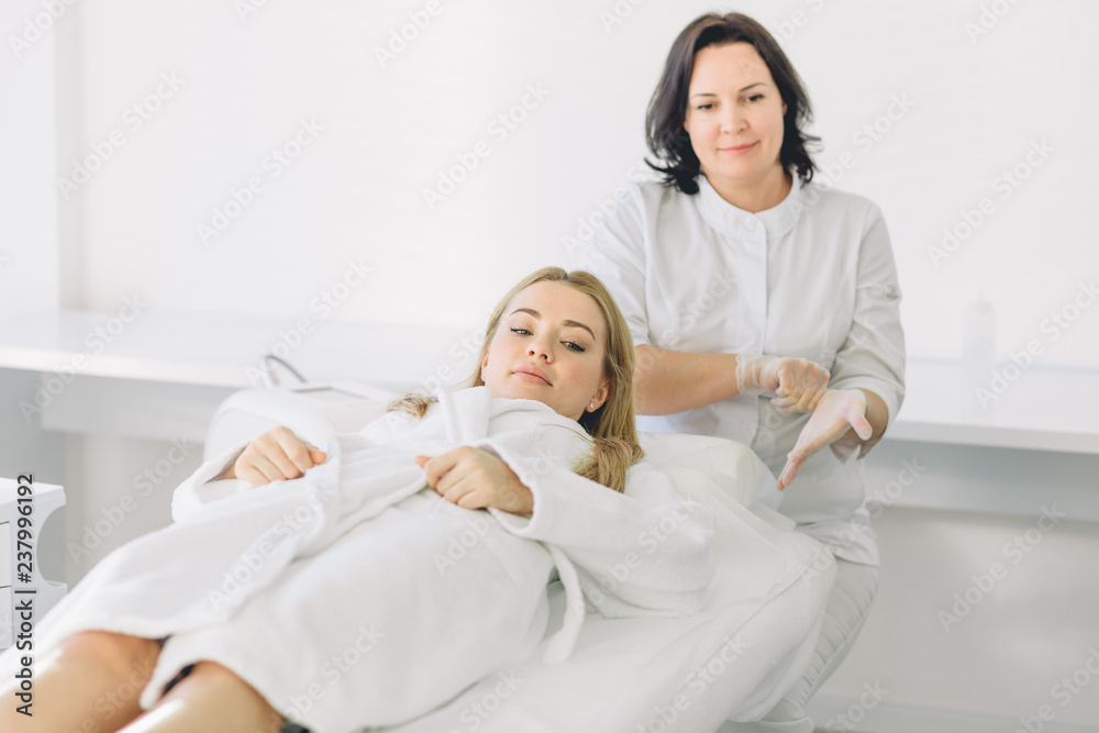 Good looking female client of spa beauty clinic, sits in white bath robe, demonstartes healthy skin, long hair, natural beauty, going to have spa treatment. Skin care Good looking female client of spa beauty clinic, sits in white bath robe, demonstartes healthy skin, long hair, natural beauty, going to have spa treatment. Skin care