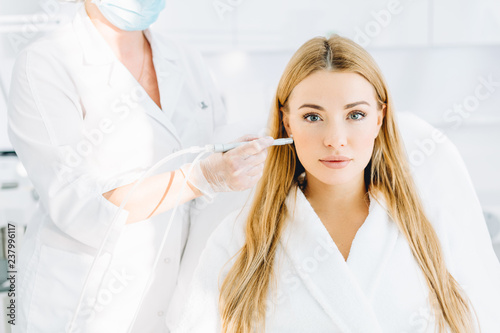 Female patient undergoing facial anti-aging procedure in beauty centre. Rejuvenating facial gas liquid treatment. Professional doctor dermatologist stroking with cosmetic apparatus woman s face skin