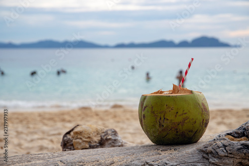 Green coconut with the straw on sea beach sand. Coconut drink on tropical seashore.