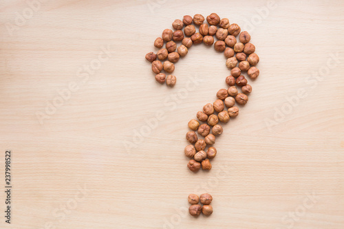 Hazelnuts in the shape of question mark on light wooden background. Hazelnuts on the table