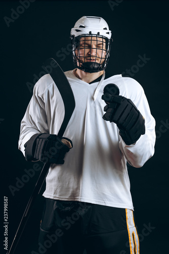 Professional caucasian hockey player holds hockey stick, looking at camera with decisive and confident look, the best team player, isolated on black