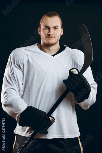 Photography Handsome caucasian hockey player posing with gaming stick at studio, looking at camera with confident look, isolated over black background