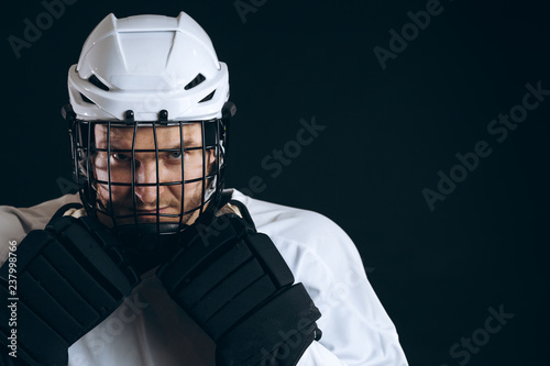 Photography Young ice-hockey sportsman in protective helmet and black hockey gloves posing over black background