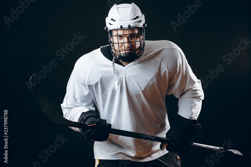 Photography Young ice-hockey sportsman in protective helmet and black hockey gloves posing over black background