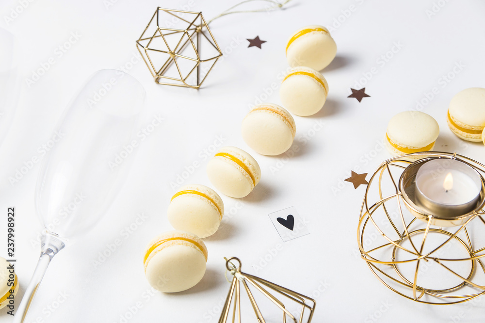 Yellow lemon macaroons on a white background next to champagne glasses. Festive gourmet Christmas aperitif. Top view, flat lay Yellow lemon macaroons on a white background next to champagne glasses. Festive gourmet Christmas aperitif. Top view, flat lay