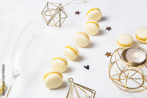 Fototapeta Naklejka Na Ścianę i Meble -  Yellow lemon macaroons on a white background next to champagne glasses. Festive gourmet Christmas aperitif. Top view, flat lay