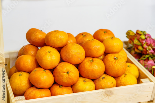 Tangerines with leaves and twigs are in a wooden box in the store on the shelf.