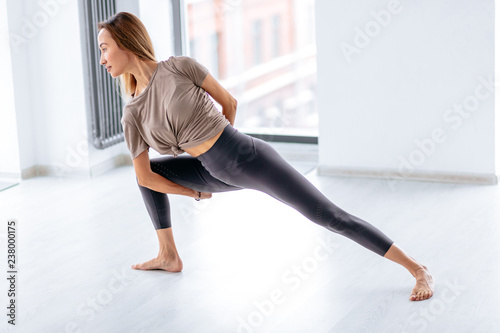 flexible girl leaning on her leg and crossing her rams behind the back. flexibility concept. side view full length photo