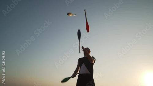 Juggler man throwing clubs against blue sky shaky footage slow motion