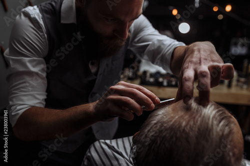Caucasin old man getting his beard shaved by barber visiting hairtician at shaving saloon, close up photo