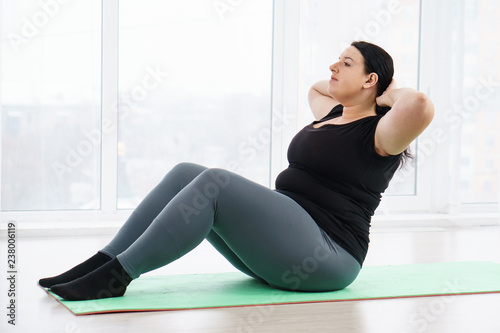 fitness, sport, weight loss, exercising, home workout, training, lifestyle. young plus size woman doing sit-ups on mat at home