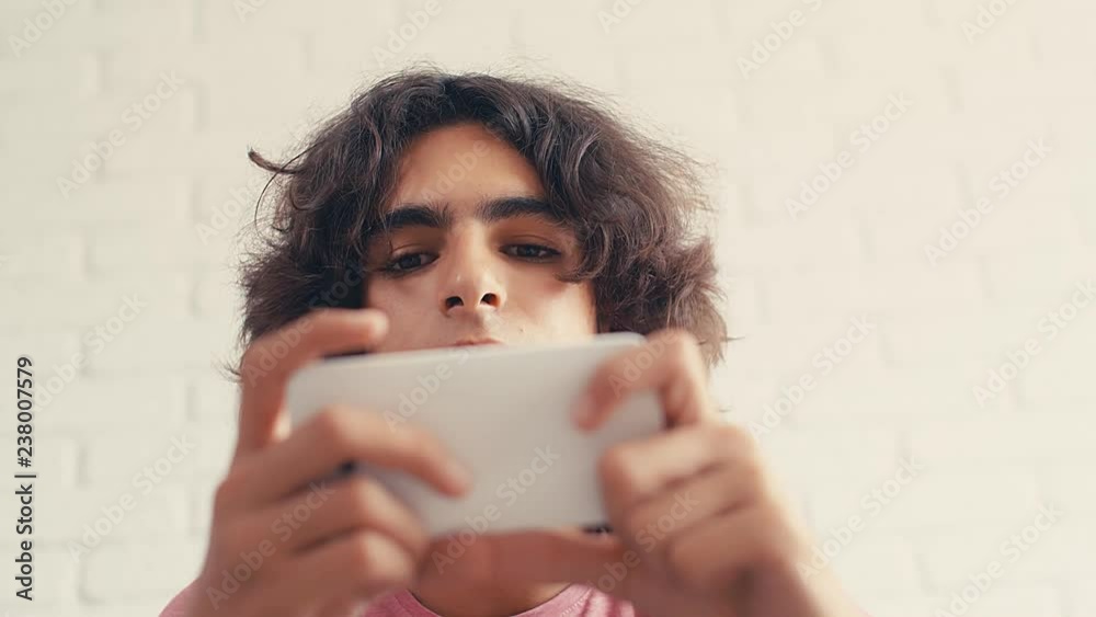 4K Teenager boy expressing positive reaction while watching something at his phone at home 4K Teenager boy expressing positive reaction while watching something at his phone at home
