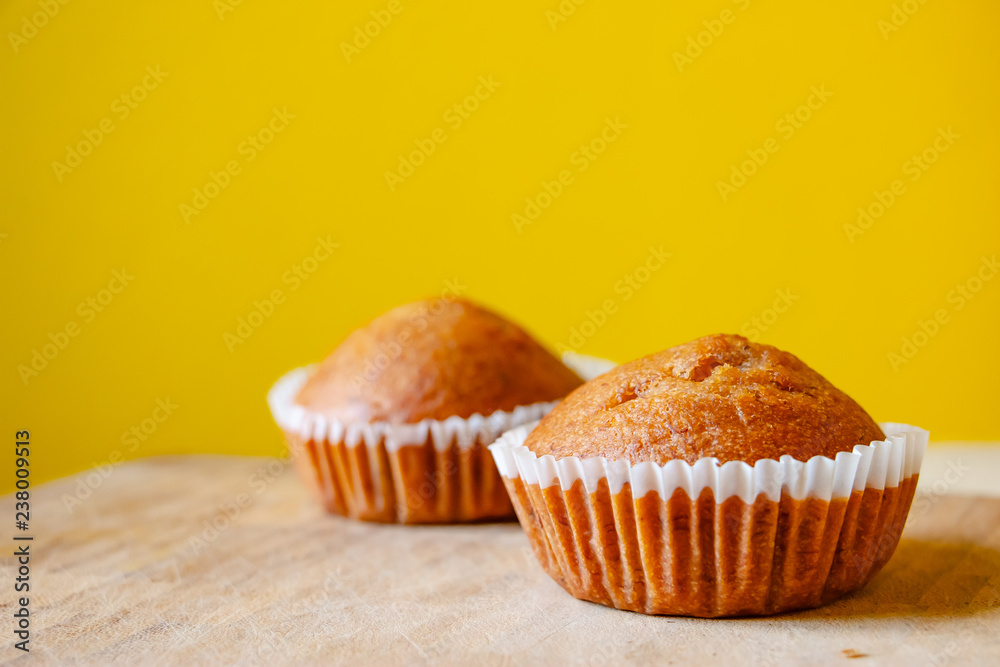 Closeup photo of the banana bread muffin in white paper cup on wooden table with yellow background. The homemade easy bake oven cake. Closeup photo of the banana bread muffin in white paper cup on wooden table with yellow background. The homemade easy bake oven cake.