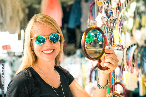 joung beautiful blond woman on the market are looking for some gifs, sunglasses and bags. she is shopping on a sunny day in italy on her travel photo