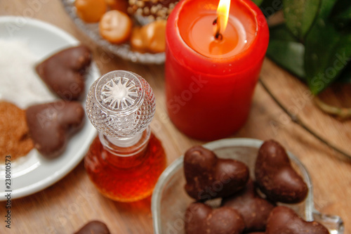 Bottle of perfume and various of cookies on wooden table with red candle. Home liana in the background. Close up.