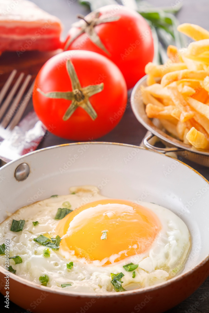 Fried egg in a pan, bacon, french fries tomatoes and green onions are cooked for breakfast on a wooden gray table. Close-up Fried egg in a pan, bacon, french fries tomatoes and green onions are cooked for breakfast on a wooden gray table. Close-up