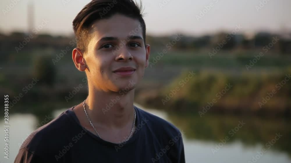 young handsome man looking at camera near the pond at sunset