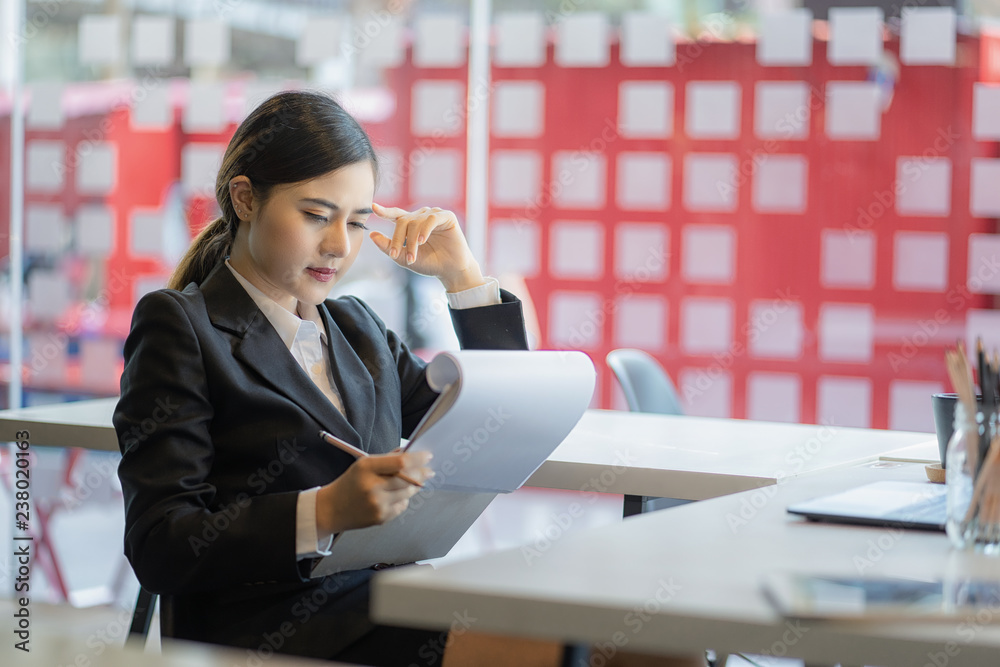 young businesswoman sitting at her desk in an office reading report on paper young businesswoman sitting at her desk in an office reading report on paper