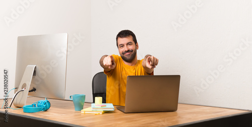 Man working with laptot in a office points finger at you while smiling