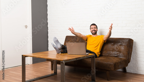 Man with his laptop in a room presenting and inviting to come with hand