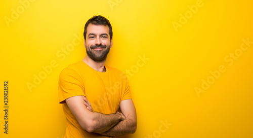 Man on isolated vibrant yellow color keeping the arms crossed in lateral position while smiling