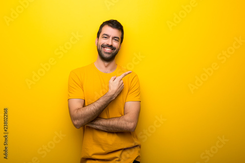 Man on isolated vibrant yellow color pointing to the side to present a product