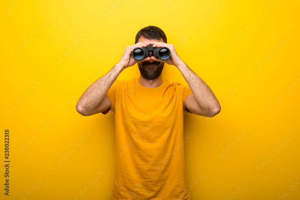 Man on isolated vibrant yellow color and looking for something in the distance with binoculars Man on isolated vibrant yellow color and looking for something in the distance with binoculars