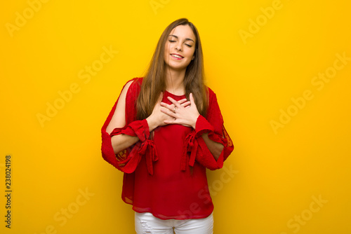 Young girl with red dress over yellow wall having a pain in the heart