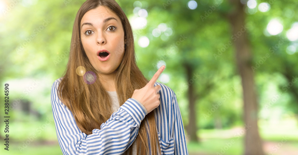 Young girl with striped shirt surprised and pointing side at outdoors Young girl with striped shirt surprised and pointing side at outdoors
