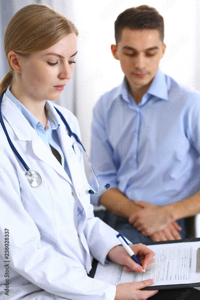 Female doctor holding application form while consulting man patient in hospital office. Medicine and healthcare concept Female doctor holding application form while consulting man patient in hospital office. Medicine and healthcare concept