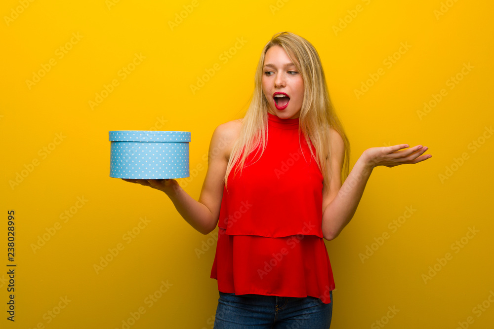 Young girl with red dress over yellow wall holding gift box in hands Young girl with red dress over yellow wall holding gift box in hands