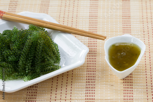 Sea grapes or green caviar and spicy sauce on a white dish the wooden dish made of Japanese style bamboo photo