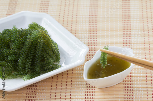 Sea grapes or green caviar and spicy sauce on a white dish the wooden dish made of Japanese style bamboo photo