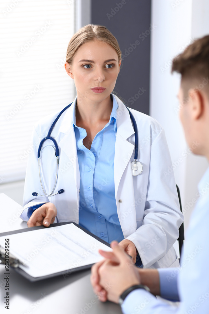 Doctor and patient in hospital. Beautiful blonde physician consulting business man about his health. Medicine concept Doctor and patient in hospital. Beautiful blonde physician consulting business man about his health. Medicine concept