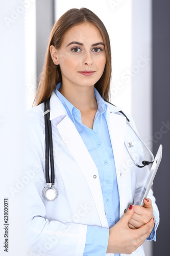 Doctor woman using tablet computer while standing straight near window in hospital. Happy physician at work. Medicine and health care concept photo